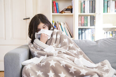 Sick girl sitting on the couch at home blowing nose - LVF06797