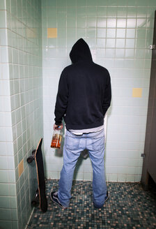 Rückansicht eines Mannes, der eine Bierflasche hält, während er eine öffentliche Toilette benutzt - CAVF11885