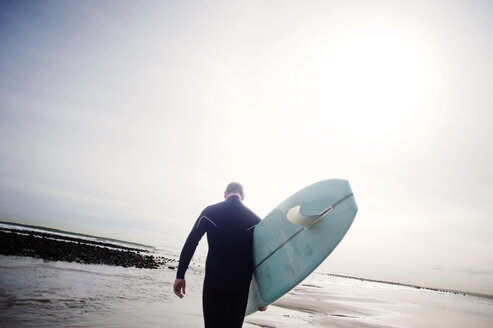 Rückansicht eines Mannes, der ein Surfbrett trägt, während er am Ufer gegen den Himmel läuft - CAVF11961