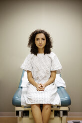 Porträt einer Frau mit verschränkten Händen auf einem Bett im Krankenhaus sitzend - CAVF11973