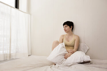 Woman looking away while sitting on bed at home - CAVF11978
