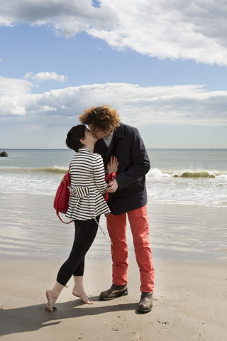 Zärtliches Paar, das sich küsst, während es am Ufer des Strandes steht, lizenzfreies Stockfoto