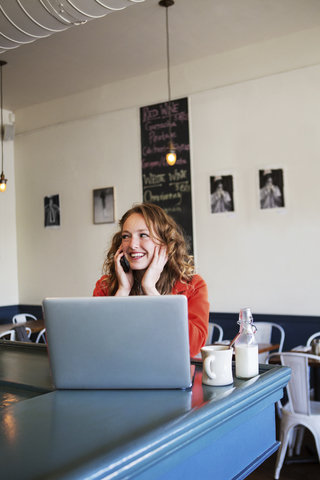 Lächelnde Frau, die in einem Café mit einem Smartphone telefoniert, lizenzfreies Stockfoto