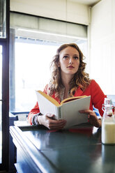 Frau mit Buch, die in einem Cafe wegschaut - CAVF12005