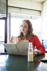 Frau liest ein Buch und trinkt Milch in einem Café - CAVF12006