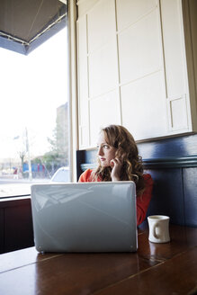 Frau mit Laptop, die in einem Café sitzt und wegschaut - CAVF12007