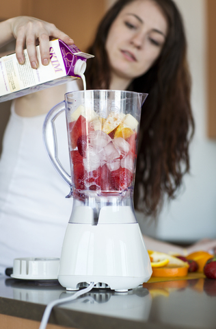 Frau gießt Milch in den Mixer, während sie zu Hause Fruchtsaft zubereitet, lizenzfreies Stockfoto