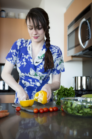 Frau schneidet gelbe Paprika, während sie in der Küche zu Hause steht, lizenzfreies Stockfoto