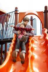 Playful father and daughter sitting on slide - CAVF12054