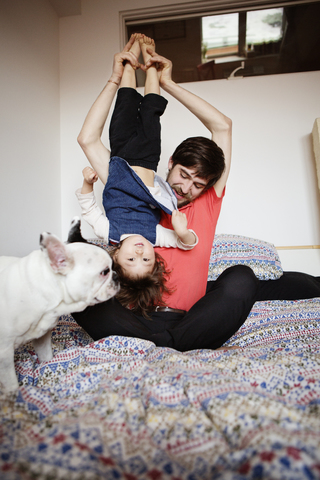 Vater trägt seine Tochter auf dem Kopf, während er neben dem Hund auf dem Bett sitzt, lizenzfreies Stockfoto