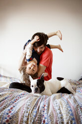 Porträt eines Vaters, der mit seiner Tochter und seinem Hund spielt, während er auf dem Bett an der Wand sitzt - CAVF12065