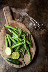 High angle view of green peas with lemon and chili pepper on cutting board by scissors at old counter - CAVF12107