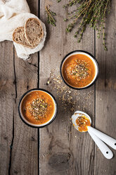 Overhead view of carrot soup in bowls with bread and rosemary on wooden table - CAVF12132