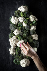Abgeschnittene Hand einer Frau, die Brokkoli und Blumenkohl auf dem Tisch berührt - CAVF12157