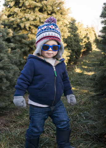 Niedlicher Junge mit Sonnenbrille steht auf einer Wiese inmitten von Kiefern, lizenzfreies Stockfoto