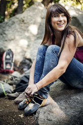 Lächelnde Frau, die auf einem Felsen sitzend Schnürsenkel bindet - CAVF12264