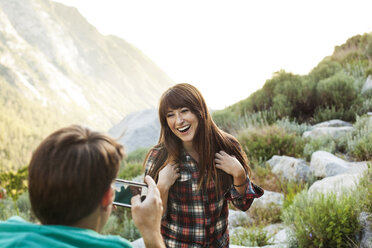 Rückansicht eines Mannes, der eine Frau mit seinem Smartphone in den Bergen fotografiert - CAVF12269