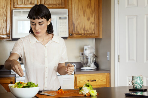 Woman seasoning salad while standing at kitchen in home - CAVF12278