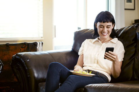Lächelnde Frau, die auf dem Sofa zu Hause sitzt und telefoniert, lizenzfreies Stockfoto