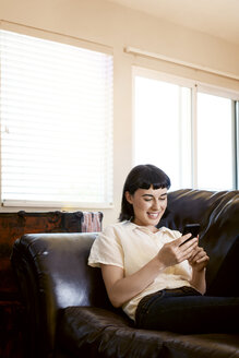 Lächelnde Frau beim Telefonieren und Entspannen auf dem Sofa zu Hause - CAVF12282