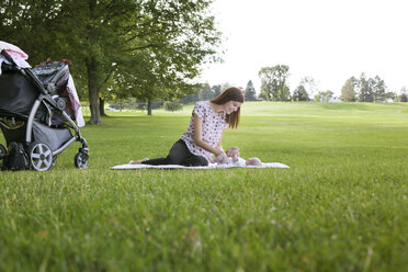 Mother playing with baby while resting on grassy field at park - CAVF12286