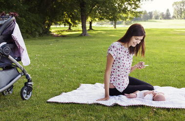 Mutter telefoniert und spielt mit Baby auf einer Wiese im Park - CAVF12289