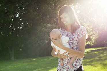 Glückliche Mutter mit Baby im Arm im Park an einem sonnigen Tag - CAVF12291