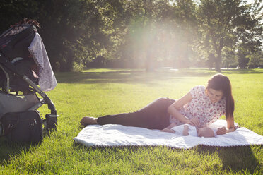 Happy mother playing with baby while resting on grassy field on sunny day - CAVF12292