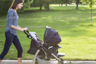 Seitenansicht einer lächelnden Frau mit Kinderwagen auf der Straße - CAVF12298