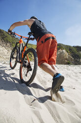 Low angle view of athlete with bicycle walking on sand against clear blue sky - CAVF12302