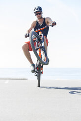 Man performing stunt with bicycle against sea on sunny day - CAVF12304