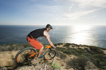 Side view of athlete riding bicycle on rock by sea - CAVF12305