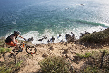 Hoher Blickwinkel eines Sportlers beim Fahrradfahren am felsigen Strand - CAVF12306
