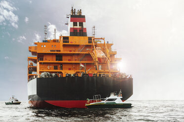 Container ship and tugboats on sea against sky - CAVF12311