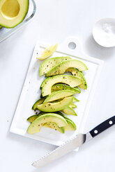 High angle view of avocado slices on cutting board over white background - CAVF12334