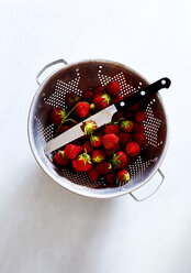 Overhead view of strawberries and kitchen knife in colander over white background - CAVF12339