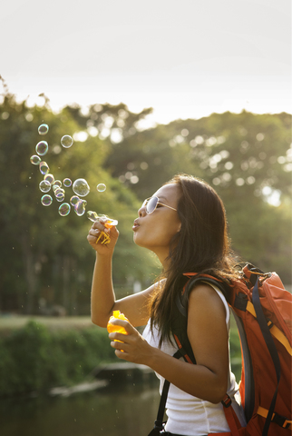 Verspielte Frau bläst Seifenblasen gegen den Himmel an einem sonnigen Tag, lizenzfreies Stockfoto