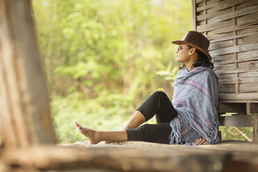 Woman wrapped in scarf relaxing by wooden cabin - CAVF12372