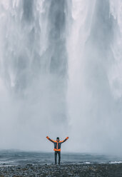 Man standing with arms outstretched against Skogafoss waterfall at Iceland - CAVF12386