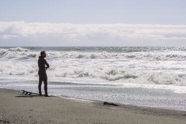 Side view of man with surfboard standing at shore against sky during sunny day - CAVF12397