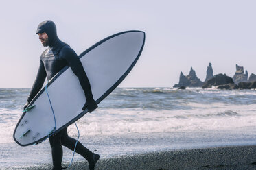 Mann mit Surfbrett zu Fuß am schwarzen Strand gegen klaren Himmel - CAVF12398