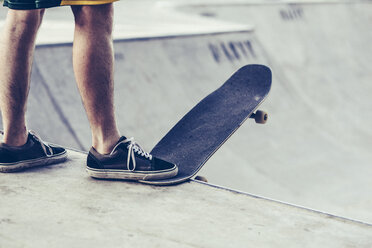 Low section of young man with skateboard at the edge of sports ramp - CAVF12409