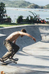 Seitenansicht eines jungen Mannes ohne Hemd, der auf einer Sportrampe Skateboard fährt - CAVF12411