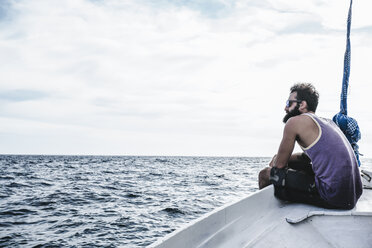 Seitenansicht eines Mannes, der auf einem Segelboot sitzt und auf das Meer blickt, bei bewölktem Himmel - CAVF12413