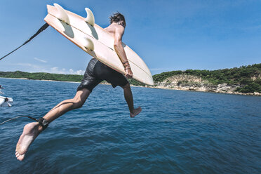 Mann mit Surfbrett springt ins Meer gegen den Himmel an einem sonnigen Tag - CAVF12419