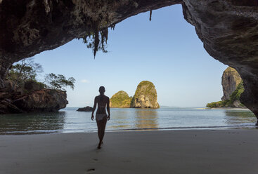 Rückansicht einer Frau im Bikini, die am Strand spazieren geht, gesehen durch eine Höhle - CAVF12423