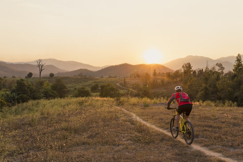 Rückansicht eines Mannes auf einem Mountainbike auf einem Feld gegen den Himmel bei Sonnenuntergang - CAVF12426