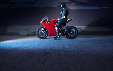 Seitenansicht eines Motorradfahrers, der auf einem Motorrad auf der Straße an einer Mauer sitzt - CAVF12463