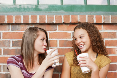 Friends enjoying drink while sitting against brick wall - CAVF12466