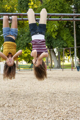 Freunde bedecken ihr Gesicht, während sie kopfüber am Klettergerüst auf dem Spielplatz hängen - CAVF12469